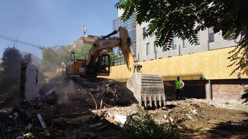Excavadora demoliendo los muros de una construcción junto a un edificio