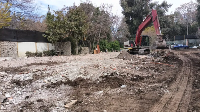 Excavadora en un terreno recién demolido, con los árboles del vecino protegidos