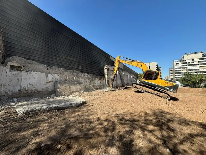 Excavadora terminando de despejar un terreno junto a un muro colindante