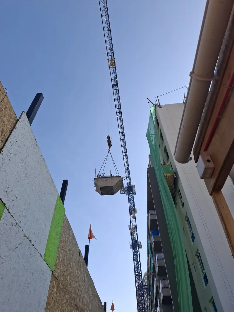Grúa torre bajando un capacho de escombros desde un edificio