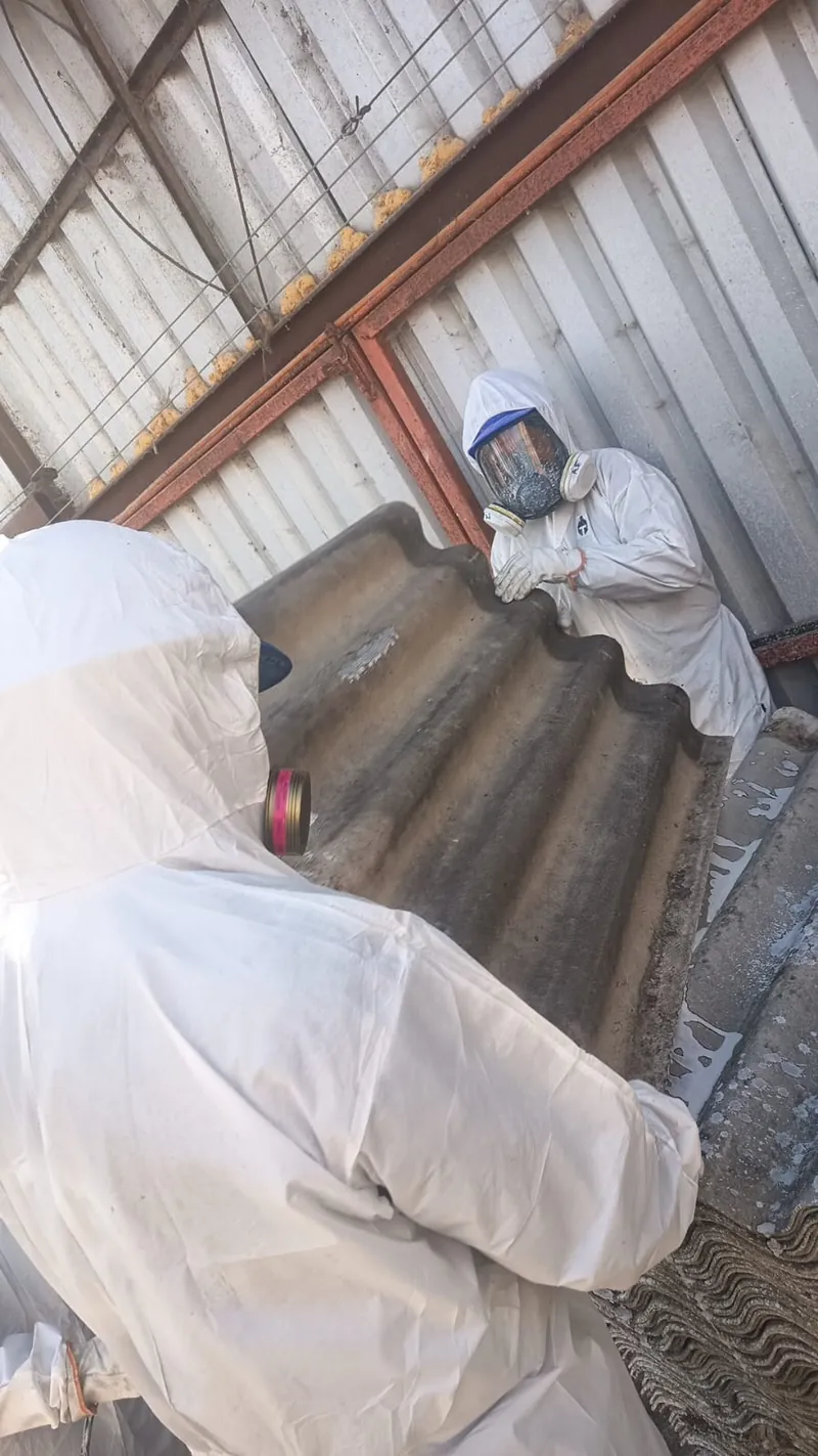 Operario con traje desechable y respirador baja una plancha de asbesto cemento