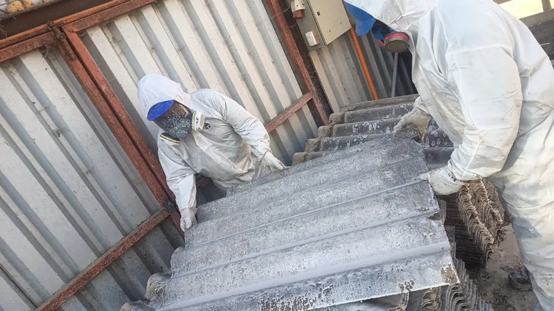 Dos operarios con traje hermético y máscara retiran planchas de fibrocemento con asbesto