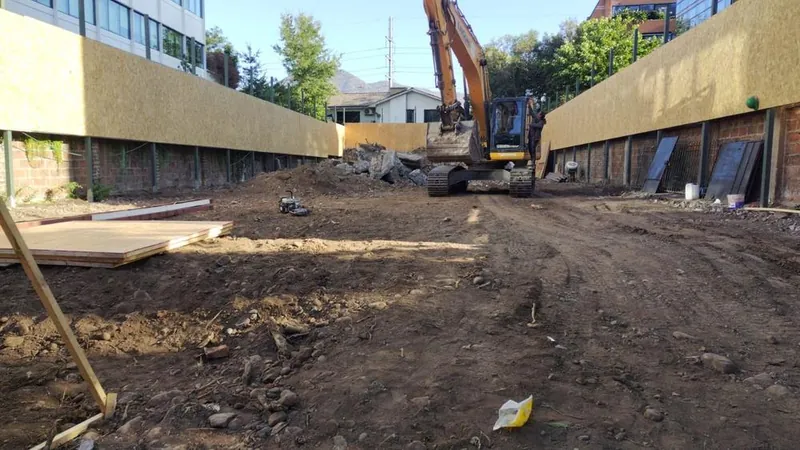 Terreno en demolición con cierre perimetral de OSB y excavadora al fondo